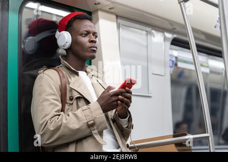 Pensive Black man in subway train thinking using cellphone listens to music with wireless headphones Stock Photo