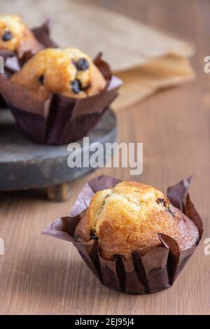 Close-up of chocolate muffin, with selective focus, on wooden table with paper bag, vertical Stock Photo