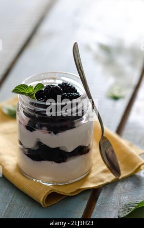 Plain yoghurt with blackberries and mint leaves in a jar on a yellow napkin and light blue wooden backdrop. Stock Photo