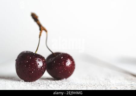 Two cherries with water drops in white wooden backdrop. Stock Photo