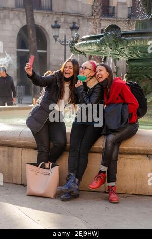 Three women friends capturing a selfie with a smart phone, smiling and sitting close together in urban environment Stock Photo