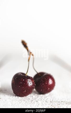 Two cherries with water drops in white wooden backdrop. Stock Photo