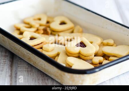 Vanilla and raspberry jam heart shaped cookies in a white tray on a white wooden backdrop. Stock Photo