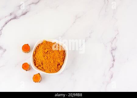 Bowl with turmeric powder with several roots of the same plant on a marble table. Concept of natural medicine and homeopathy Stock Photo