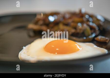 Fried egg on a black plate with veggies on the background Stock Photo