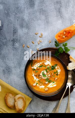 Butternut squash soup with cream, cashew and parsley, in a black bowl on a wooden plate. Stock Photo