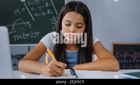 upset kid writing on notebook while doing homework Stock Photo