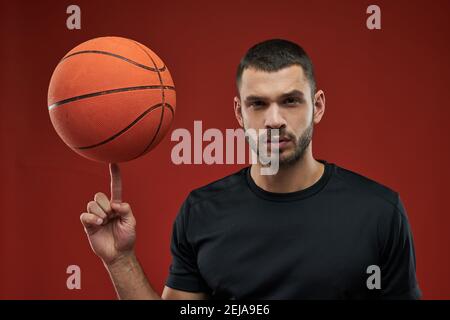 Close up portrait of handsome adorable basketball player holding basket ball on his finger in the indoors Stock Photo