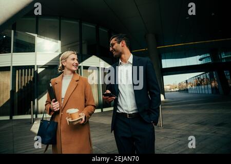Caucasian business woman and mixed race male colleague walking together chatting friendly about co-workers  Stock Photo