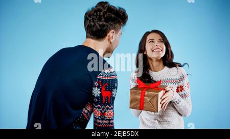 Smiling woman with present standing near boyfriend in sweater on blue background Stock Photo