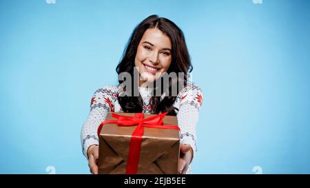 Smiling woman in sweater holding present on blue background Stock Photo