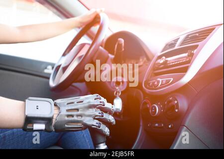 A girl with a prosthetic arm drives a car. The concept of a full life for people with disabilities. Side view, small depth of field, soft sun glare. Stock Photo