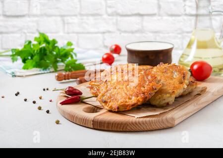 Freshly cooked potato pancakes with sour cream on a wooden board on the kitchen table. Vegetarian dish Stock Photo