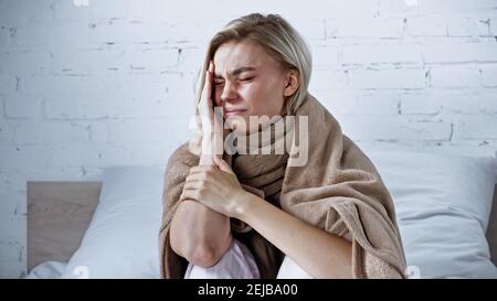 ill woman, wrapped in warm blanket, suffering from headache in bedroom Stock Photo