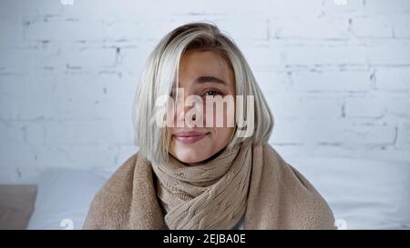 young ill woman, wrapped in blanket, smiling at camera in bedroom Stock Photo