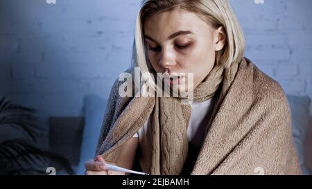 young diseased woman looking at thermometer in bedroom Stock Photo