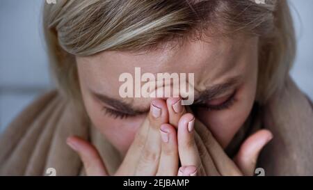 close up view of sick woman sneezing and covering nose with hands