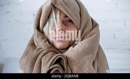 diseased woman, wrapped in warm blanket, smiling at camera in bedroom Stock Photo