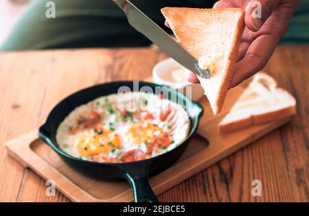 Man spreading butter on the bread with Pan Fried Egg with Toppings Stock Photo