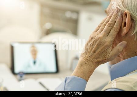 Fragment photo of elderly man touching his head while having a video online consultation with medical specialsit Stock Photo