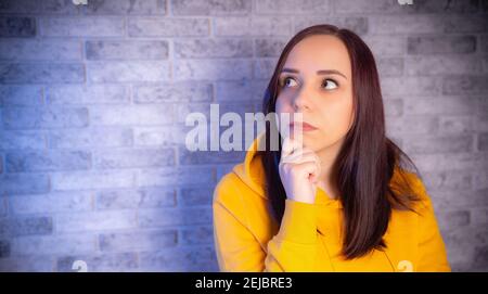Portrait of thoughtful young woman on gray brick background. Close up of cute brunette propping up her chin in reflections Stock Photo