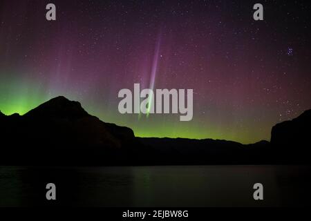 Red, Green and yellow Aurora Borealis (Northern Lights) with pillars from a lake in the Canadian Rockies during a spring night, Lake Minnewanka, Banff Stock Photo