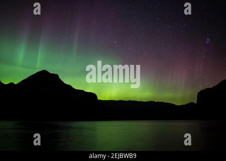 Red, Green and yellow Aurora Borealis (Northern Lights) from a lake in the Canadian Rockies during a spring night, Lake Minnewanka, Banff, Canada Stock Photo