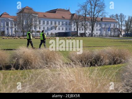 Oranienburg, Germany. 22nd Feb, 2021. Two stewards in yellow and green high-visibility vests walk along a path in mild temperatures and a cloudless sky against the backdrop of the castle in Schloßpark. The district of Oberhavel had approved the reopening of the park under strict conditions. For example, visitors must observe the distance rules and - with the exception of children under six - wear an FFP2 or medical mask. Credit: Soeren Stache/dpa-Zentralbild/ZB/dpa/Alamy Live News Stock Photo