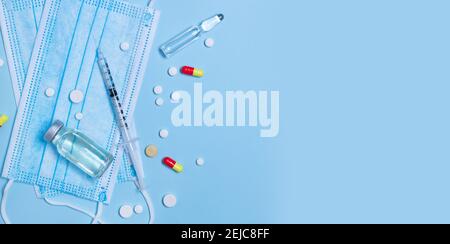 Top view medical composition of syringe with medication, antibiotic vial, pills and protective mask on blue background with copypys. Stock Photo