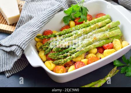 Green asparagus on Italian gnocchi with cherry tomatoes baked with grated parmesan cheese Stock Photo