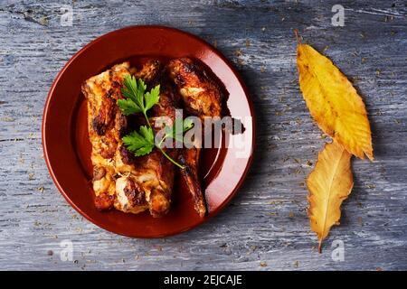 high angle view of a dark brown earthenware plate with some pieces of roast rabbit as is eaten in spain, on a rustic gray wooden table Stock Photo