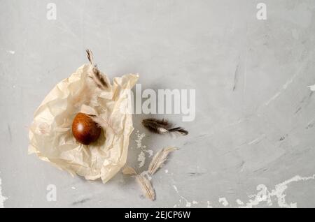 Easter background. Painted chicken egg lies on crumpled paper with feathers and on a concrete gray background, flat layout, copying text Stock Photo