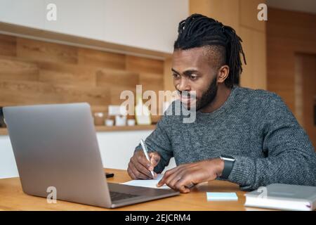 African American man student freelancer making notes working with laptop Stock Photo