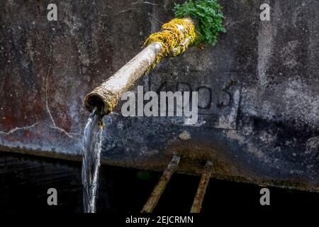 Water flowing from a rusty fountain by a weathered concrete wall , Puy de Dome , Auvergne, France Stock Photo