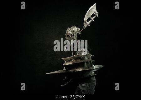 Medieval fighter in armor, in profile, carrying a shield and an ax on his shoulder, in attack position Stock Photo