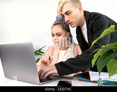 Work in the office, business. Young attractive man helping his female colleague to deal with the project. He leaned over her laptop, standing next to Stock Photo