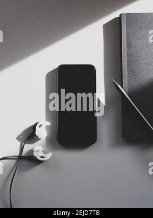 Mock up of a mobile phone, notebook and earphones on a gray table Stock Photo