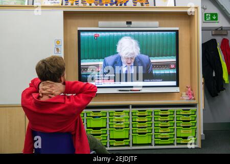 A male primary school teacher sitting in his classroom watching Prime Minister Boris Johnson on the classroom interactive smart board announce schools are to reopen to all schoolchildren in England from the 8th March. London, U.K. 22nd February, 2021. Stock Photo