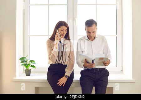 Woman talking on mobile while man is reading notes getting ready for corporate meeting Stock Photo