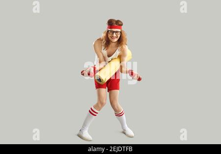 Funny skinny young man in retro sportswear doing fitness exercise with gym dumbbells Stock Photo