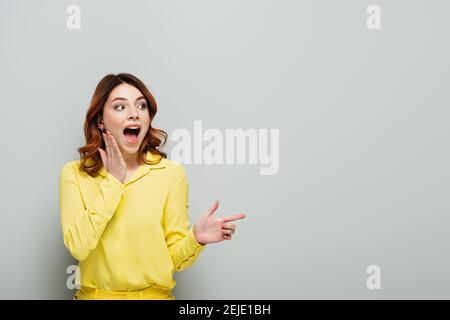 amazed young woman in yellow shirt pointing with finger and looking away on grey Stock Photo