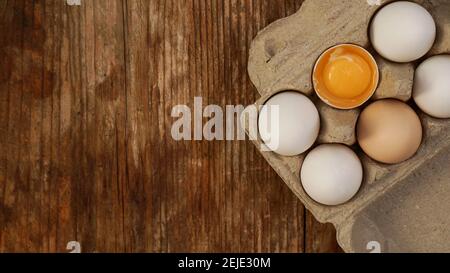 White eggs carton and cracked egg half with yolk top view on wooden background. Easter and healthy food breakfast cooking concept Stock Photo