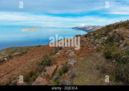 Agriculture field terraces on Isla del Sol (Sun Island) with the sunlit Moon Island, Titicaca Lake, Bolivia. Stock Photo
