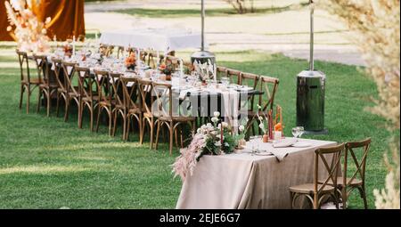 Chairs and table for newlyweds decorated with candles, served with cutlery, crockery and covered with tablecloth Stock Photo