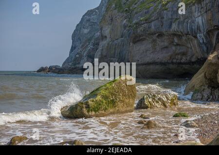 Wave splashing on the rocks at the base of the little Orme, Llandudno. North Wales pebble beach Stock Photo