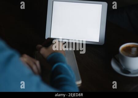 Man is sitting in a cafe and uses a tablet and write down something in the notebook Stock Photo