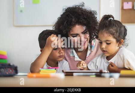 Teacher with children using digital tablet in preschool classroom - Education and technology concept Stock Photo