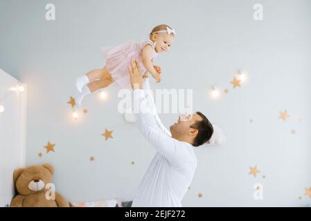 Father lifting baby girl. Happy father picks up and throws his lifting a small child. Home atmosphere, happy family laughing baby Stock Photo