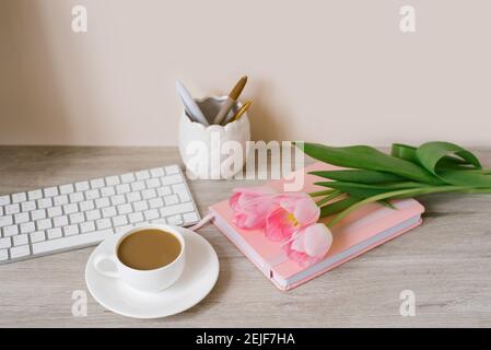 Pink tulips with a festive spring mood and coffee on a wooden table Women's work, home office and career concept. Side view Stock Photo