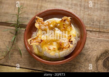 French Camembert that has been baked in an oven with a truffle, garlic and honey sauce. Wooden background garnished with rosemary. England UK GB Stock Photo
